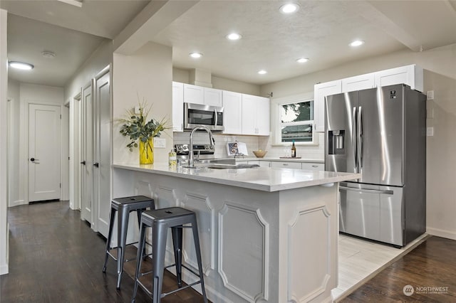 kitchen featuring kitchen peninsula, stainless steel appliances, sink, hardwood / wood-style floors, and white cabinetry