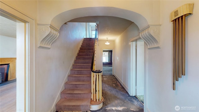 stairs with concrete floors, baseboards, and arched walkways