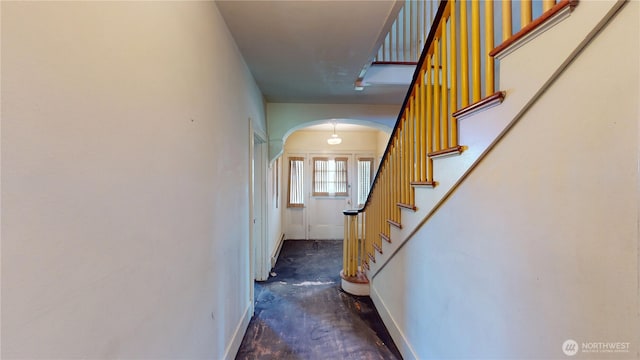 corridor with baseboards, unfinished concrete flooring, arched walkways, and stairs