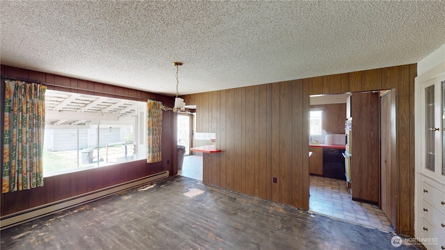 unfurnished dining area with wooden walls, a textured ceiling, a chandelier, and baseboard heating