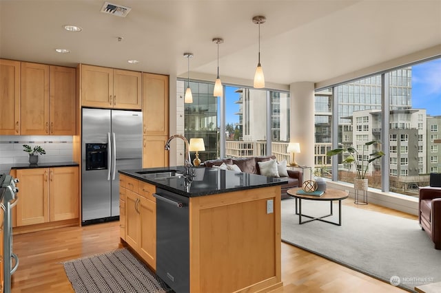 kitchen with appliances with stainless steel finishes, light wood-type flooring, sink, pendant lighting, and a center island with sink