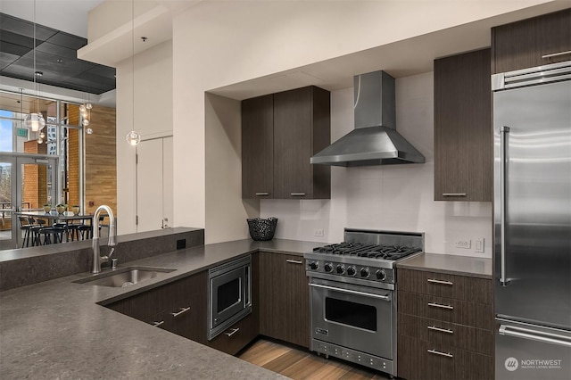 kitchen featuring light wood-type flooring, wall chimney exhaust hood, dark brown cabinets, premium appliances, and sink