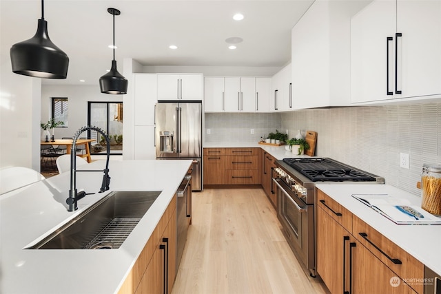 kitchen with sink, decorative light fixtures, premium appliances, white cabinets, and backsplash