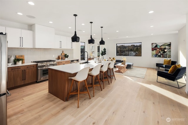 kitchen with double oven range, a kitchen island with sink, wall chimney range hood, and light wood-type flooring