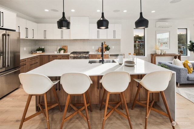 kitchen featuring pendant lighting, a wall mounted air conditioner, stainless steel appliances, and a center island with sink