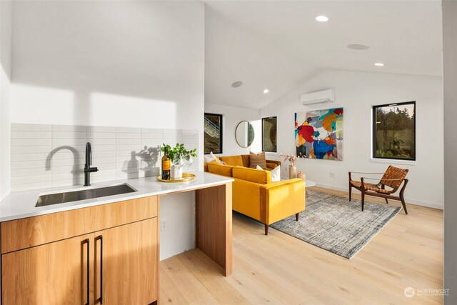 kitchen with a wall mounted air conditioner, light hardwood / wood-style floors, sink, and backsplash