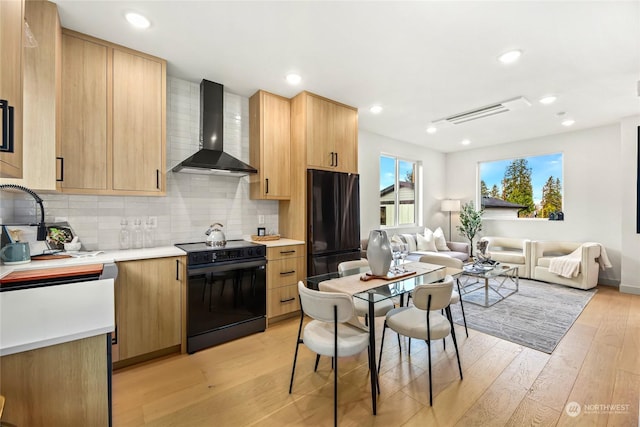 kitchen with backsplash, light brown cabinets, black appliances, wall chimney range hood, and light wood-type flooring