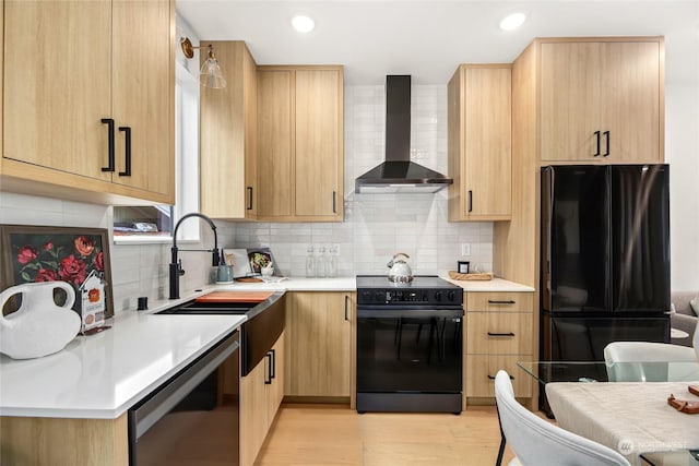 kitchen featuring light brown cabinetry, wall chimney range hood, and black appliances