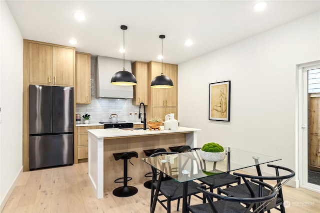 kitchen featuring light brown cabinetry, refrigerator, tasteful backsplash, decorative light fixtures, and light hardwood / wood-style flooring