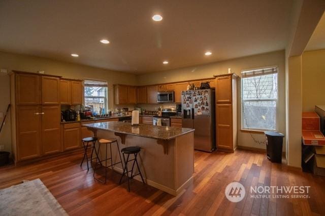 kitchen with hardwood / wood-style flooring, a kitchen island, appliances with stainless steel finishes, and dark stone counters