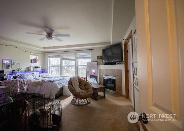 bedroom with a raised ceiling, light carpet, a fireplace, and ceiling fan