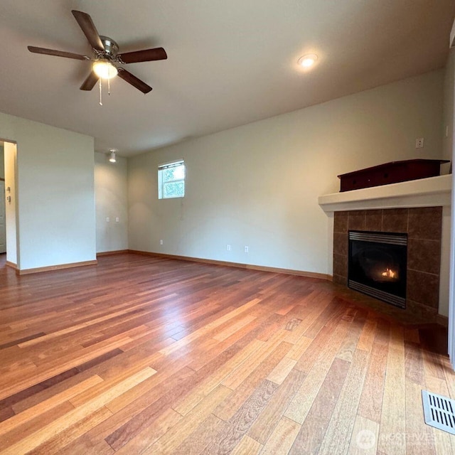 unfurnished living room with a tiled fireplace, visible vents, baseboards, and hardwood / wood-style flooring