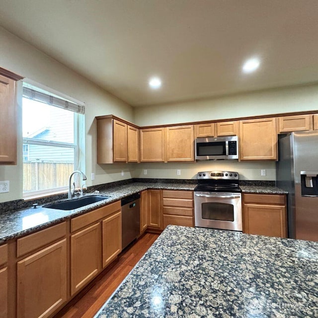 kitchen with dark wood-style flooring, appliances with stainless steel finishes, dark stone counters, and a sink