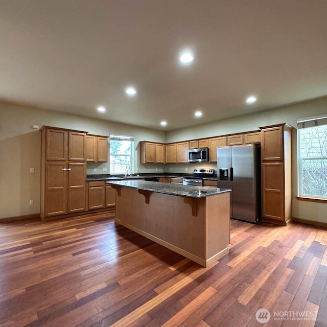 kitchen with stainless steel appliances, a kitchen breakfast bar, dark wood finished floors, and a center island