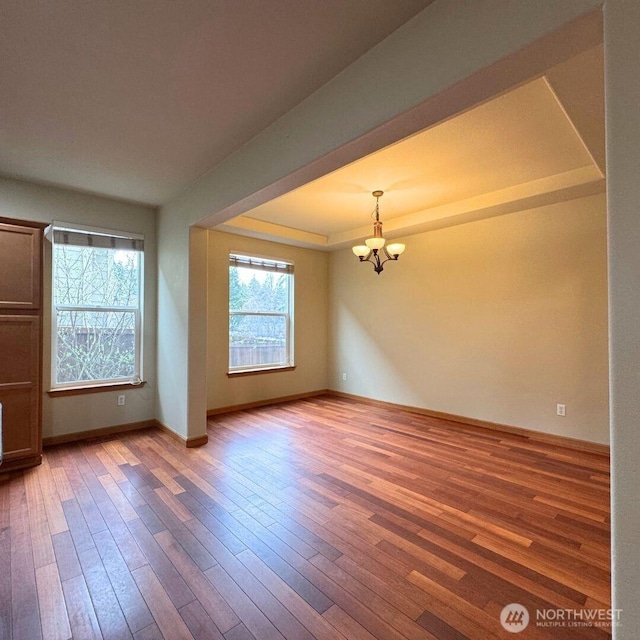 empty room featuring a raised ceiling, a notable chandelier, wood finished floors, and baseboards