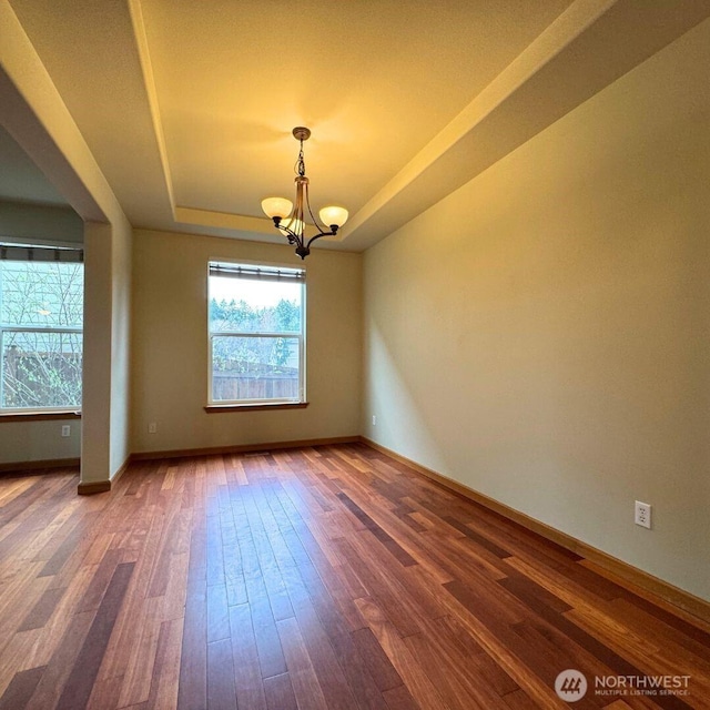 spare room with a chandelier, baseboards, a tray ceiling, and wood finished floors