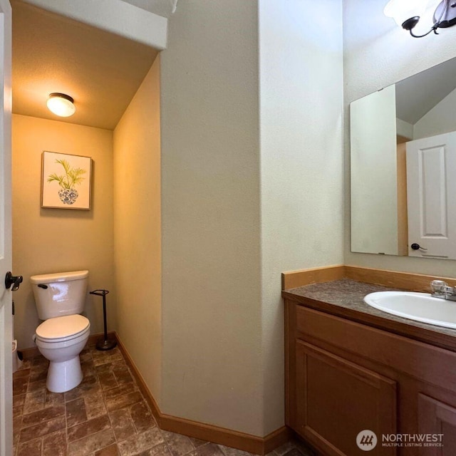 bathroom featuring baseboards, toilet, vanity, and stone finish floor