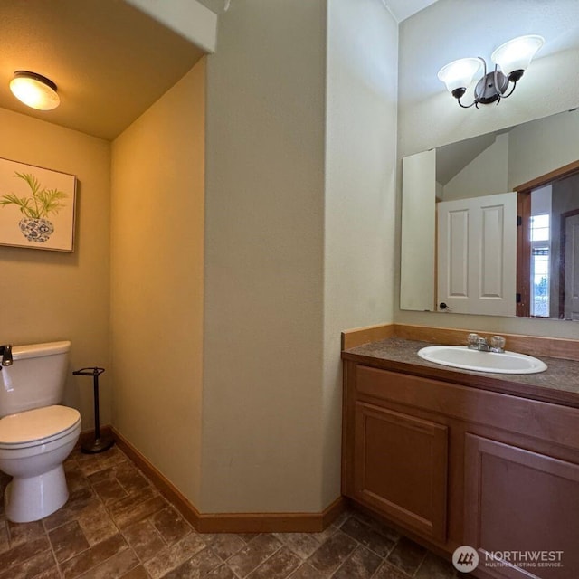 half bathroom with stone finish flooring, baseboards, toilet, and vanity