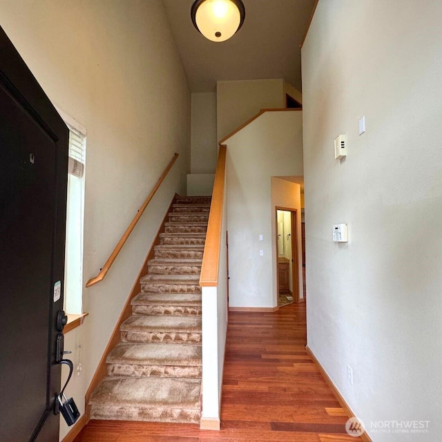 stairway with wood finished floors and a towering ceiling