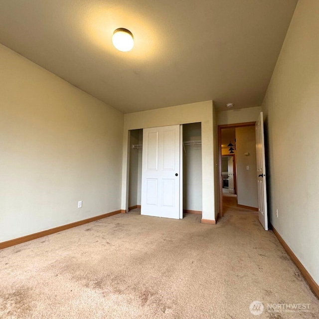 unfurnished bedroom with a closet, light colored carpet, and baseboards