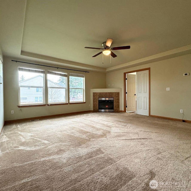 unfurnished living room with ceiling fan, baseboards, a tiled fireplace, carpet, and a raised ceiling