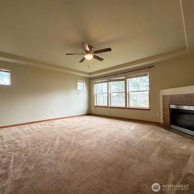 unfurnished living room with carpet flooring, a raised ceiling, a fireplace with flush hearth, and baseboards