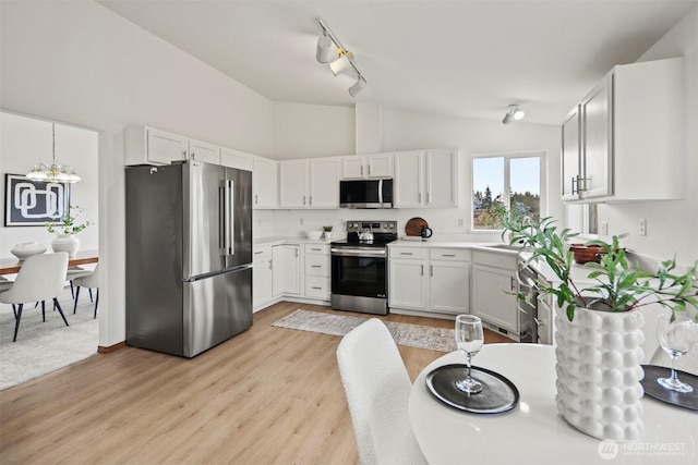 kitchen featuring light wood finished floors, lofted ceiling, stainless steel appliances, light countertops, and a sink