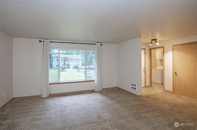 empty room with a textured ceiling, light carpet, and washer / clothes dryer