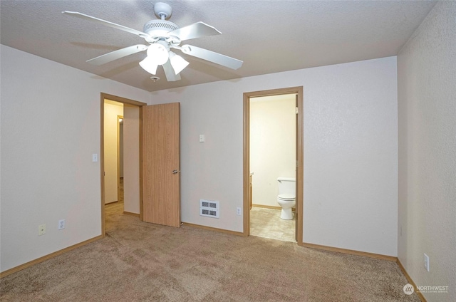 unfurnished bedroom with light carpet, heating unit, ensuite bathroom, and ceiling fan