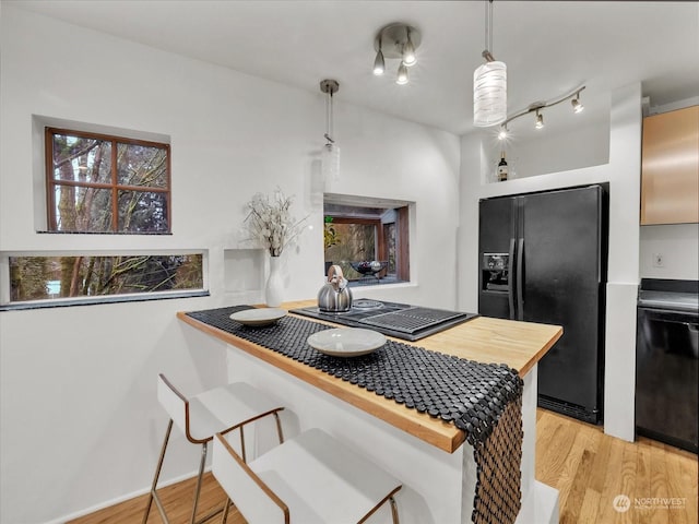 kitchen with kitchen peninsula, pendant lighting, black appliances, and light hardwood / wood-style flooring