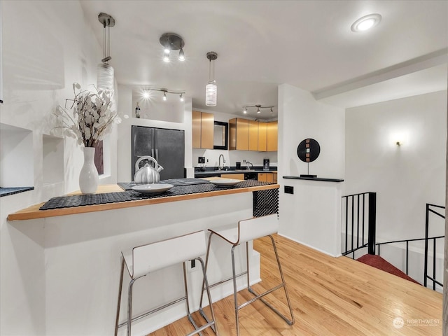 kitchen with kitchen peninsula, a kitchen bar, light wood-type flooring, light brown cabinets, and fridge