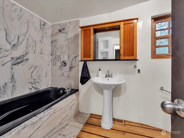 bathroom featuring crown molding, sink, and tiled tub