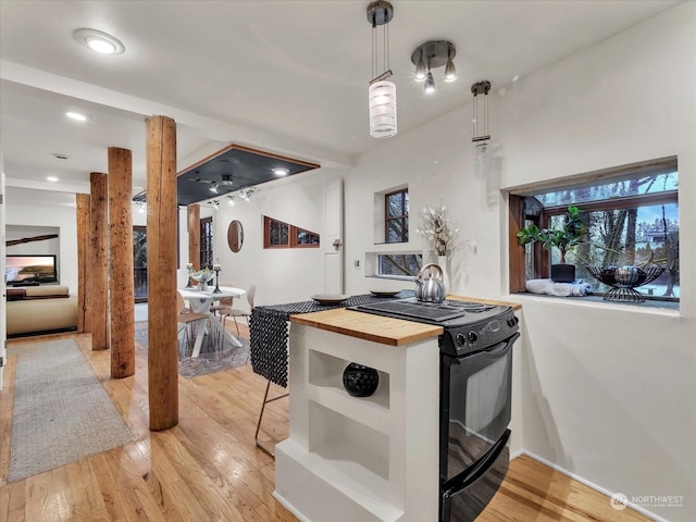 kitchen featuring wooden counters, black range oven, hanging light fixtures, light hardwood / wood-style flooring, and a breakfast bar area