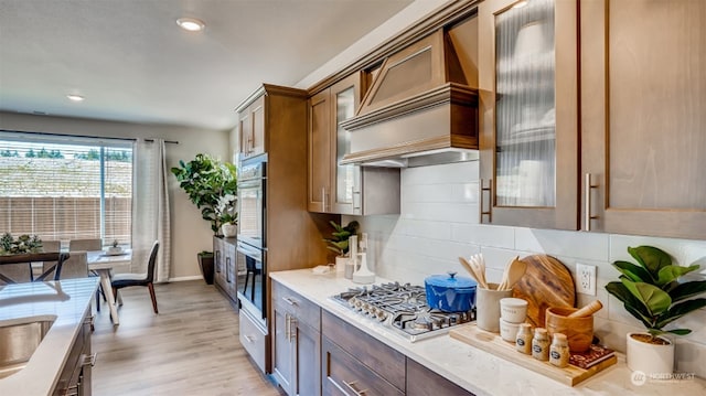 kitchen featuring light stone countertops, stainless steel gas cooktop, backsplash, light hardwood / wood-style floors, and custom range hood