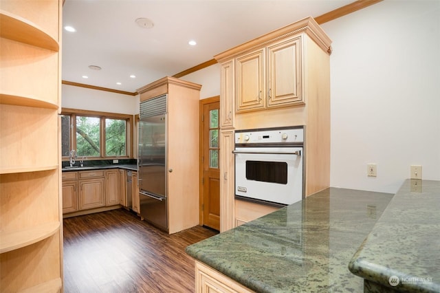 kitchen with oven, sink, dark hardwood / wood-style floors, ornamental molding, and stainless steel built in refrigerator