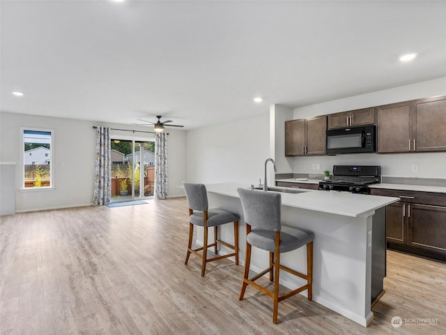 kitchen featuring a kitchen bar, ceiling fan, sink, black appliances, and an island with sink