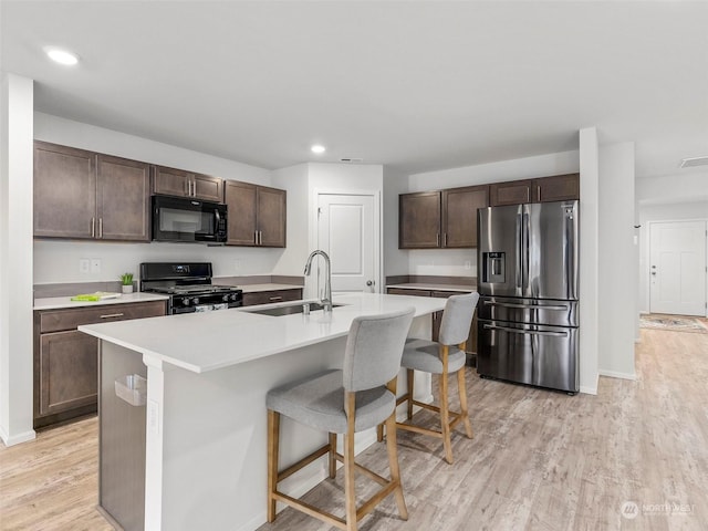 kitchen featuring dark brown cabinetry, sink, an island with sink, a kitchen bar, and black appliances