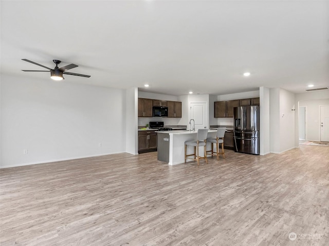 kitchen featuring black appliances, a breakfast bar, a center island with sink, and light hardwood / wood-style flooring