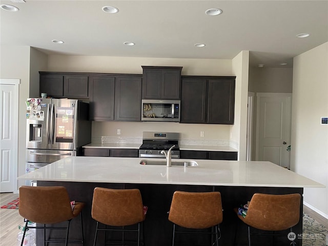 kitchen featuring sink, light hardwood / wood-style flooring, a kitchen island with sink, a breakfast bar, and appliances with stainless steel finishes