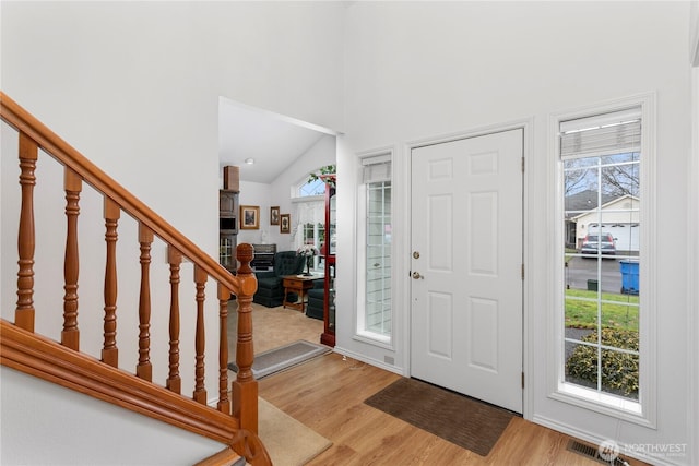 entryway with stairs, high vaulted ceiling, and light wood-style flooring