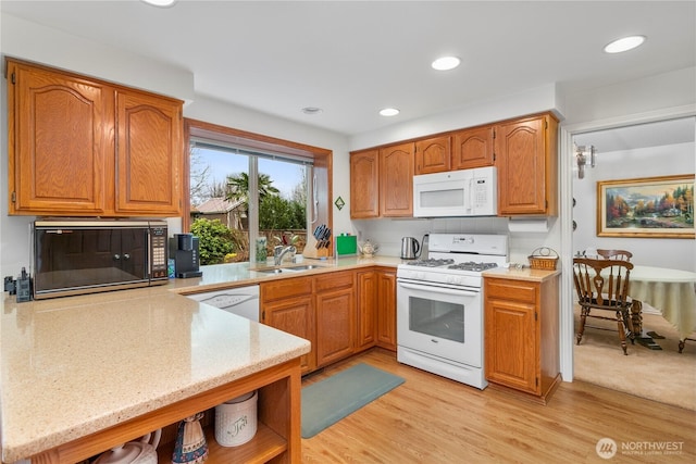 kitchen with brown cabinetry, a sink, light stone counters, light wood finished floors, and white appliances
