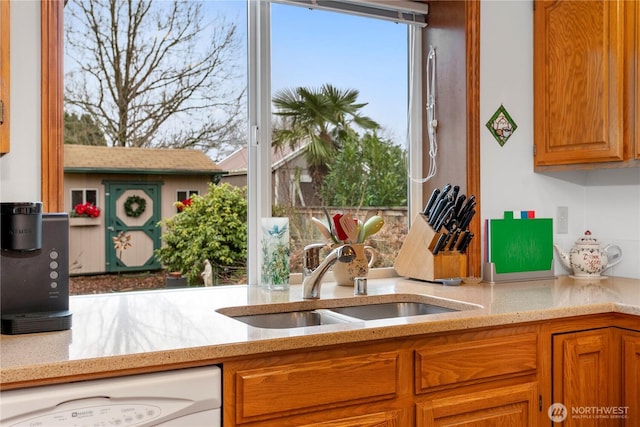 kitchen featuring brown cabinetry, a sink, dishwasher, and light stone countertops