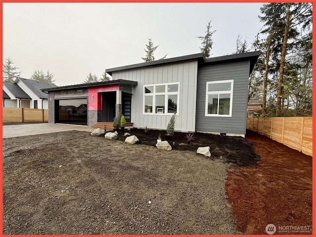 contemporary home featuring a garage, driveway, board and batten siding, and fence