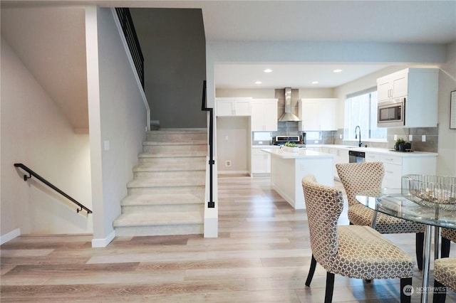 kitchen featuring white cabinets, appliances with stainless steel finishes, a kitchen island, wall chimney range hood, and light wood-type flooring