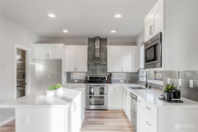 kitchen with white cabinetry, appliances with stainless steel finishes, wall chimney range hood, a kitchen island, and sink