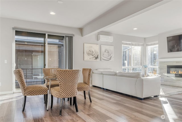 dining space featuring a wall unit AC, a tile fireplace, and light hardwood / wood-style flooring