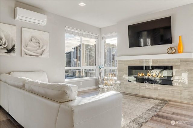 living room featuring a wall mounted AC, a tiled fireplace, and wood-type flooring