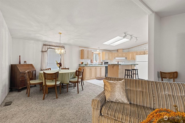 carpeted dining room featuring a textured ceiling, an inviting chandelier, and lofted ceiling with skylight