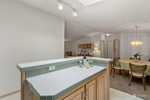 kitchen featuring a center island, vaulted ceiling, light brown cabinets, and an inviting chandelier