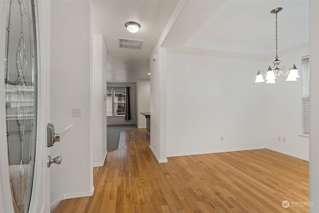 corridor with light hardwood / wood-style floors, a raised ceiling, and an inviting chandelier